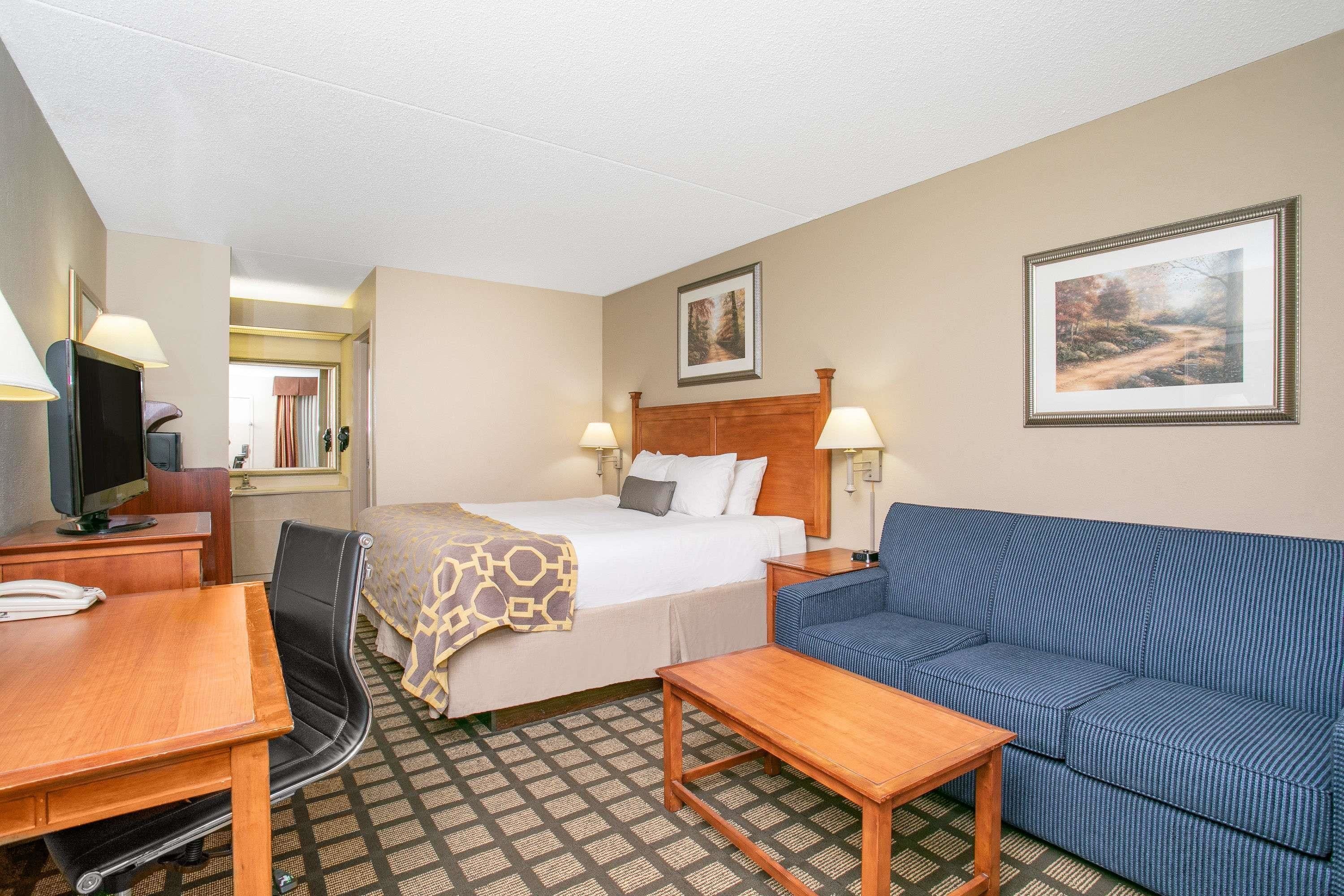 A hotel room with a bed, a blue sofa, a wooden table, a desk with a telephone, and two wall-mounted lamps.