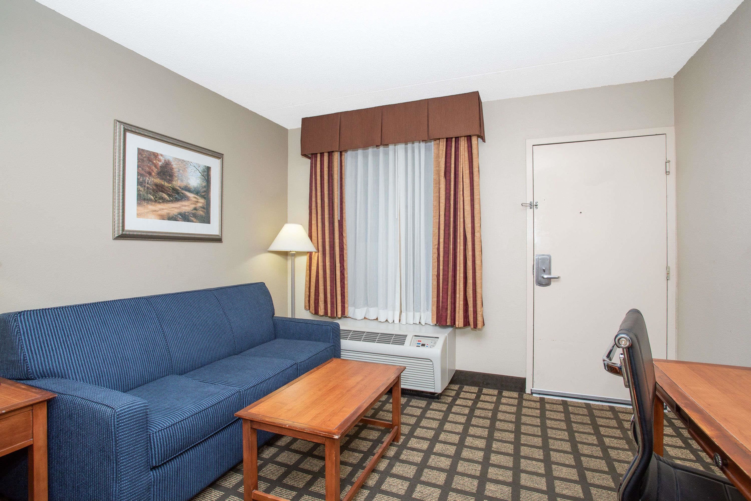 A hotel room with a blue sofa, a wooden table, a lamp, an air conditioner, and a door.