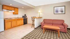 A compact living space with a kitchenette, a sofa, a small table, and a lamp. - Baymont by Wyndham Hays (Hays)
