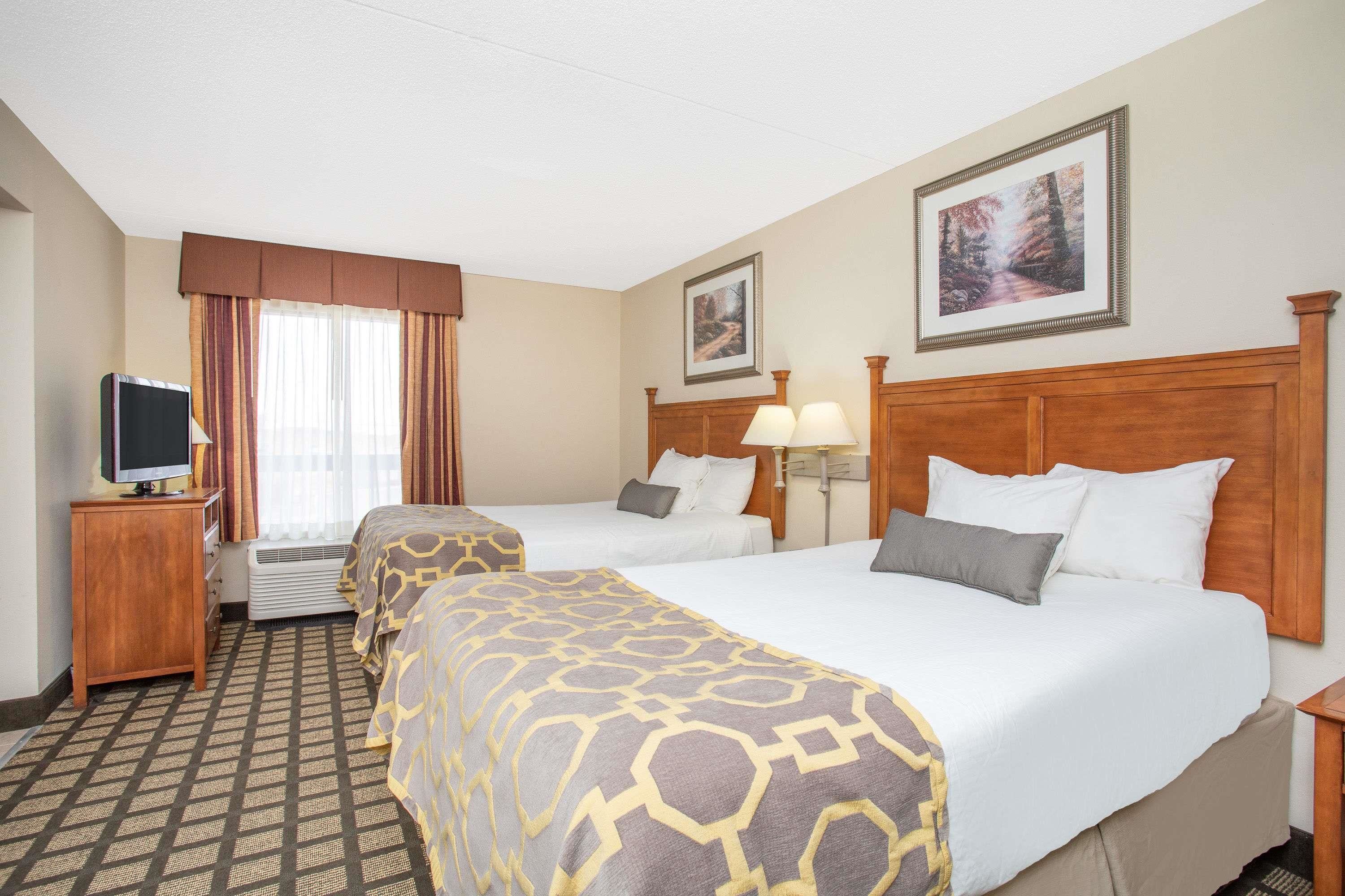 A hotel room with two beds, a television, a window with curtains, and framed pictures on the wall.