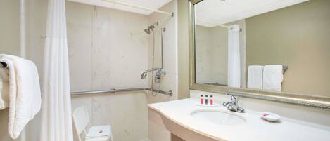 A bathroom with a shower, a sink, a mirror, and a chair.