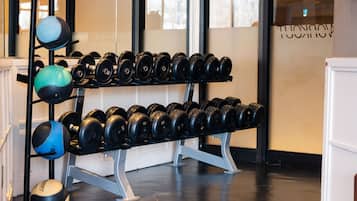 Un gimnasio con equipo de levantamiento de pesas, incluyendo mancuernas y kettelbells, organizadas en estanterías.