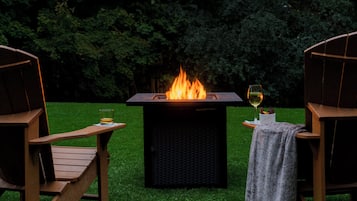 A wooden deck with two chairs and a square fire pit with flames.