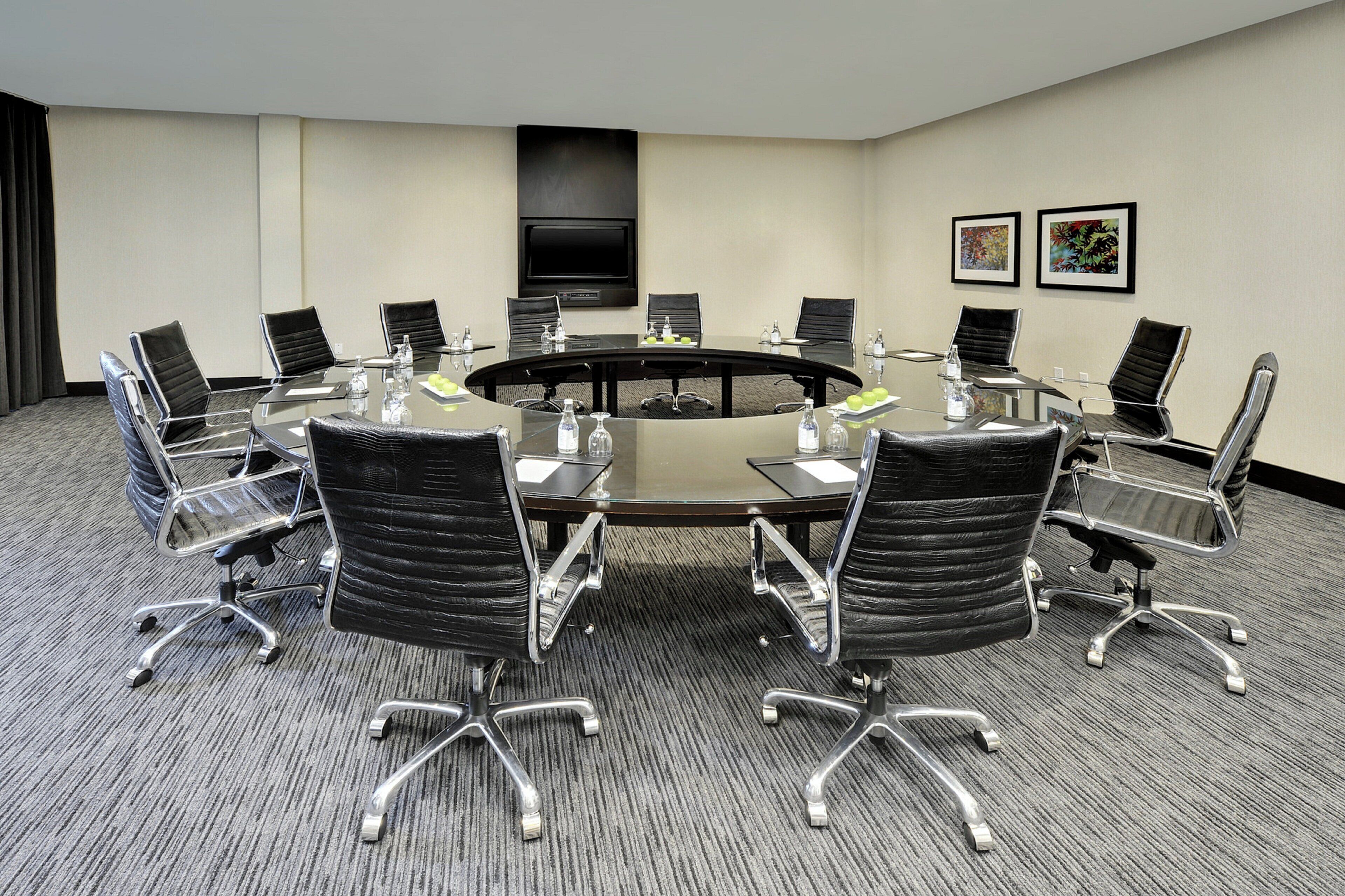 A conference room with a round table, black leather chairs, and a flat-screen TV on the wall.
