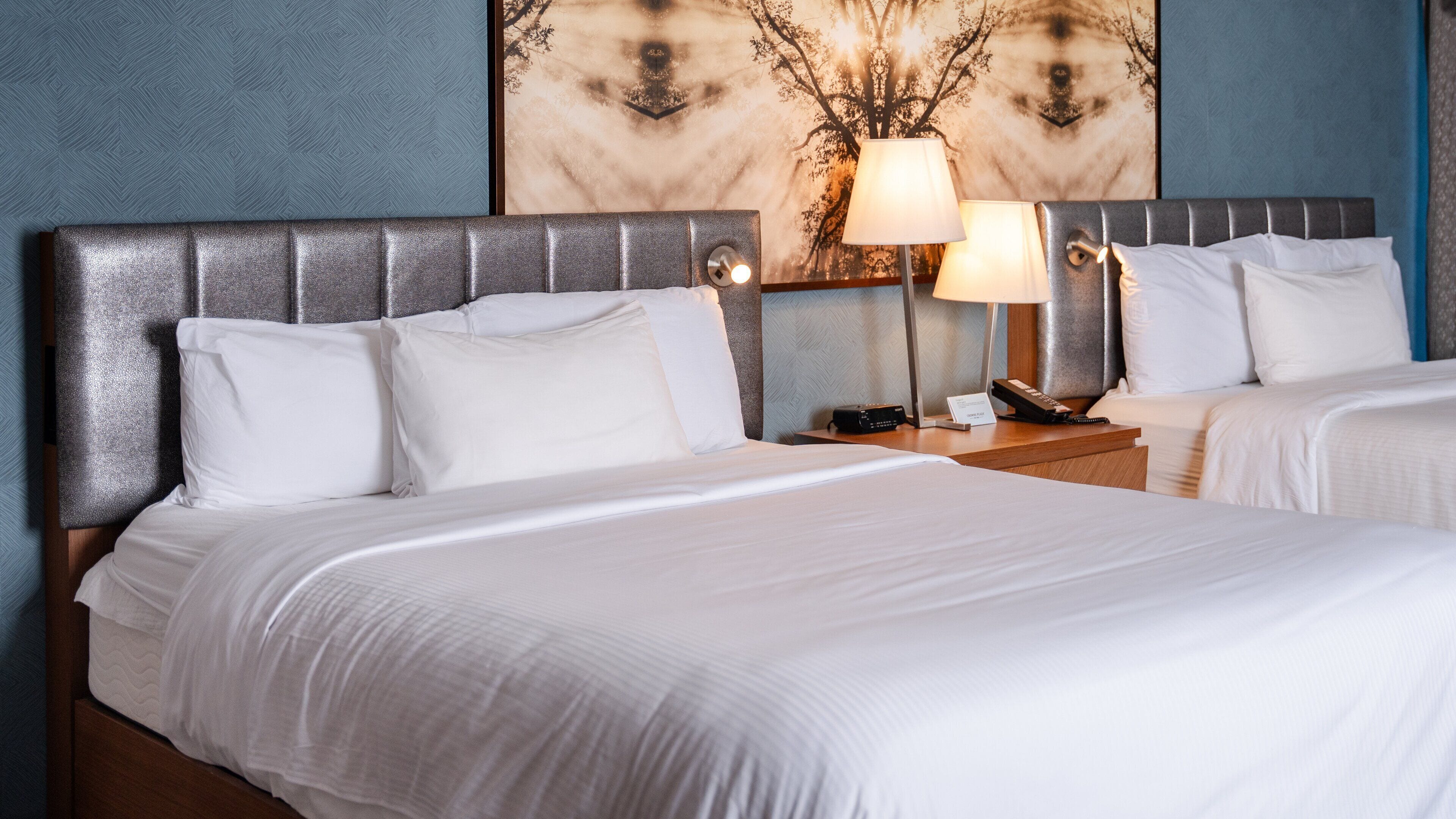 A hotel room with a large bed, two bedside tables, a lamp, and a wall with a tree design.