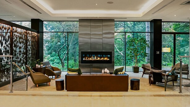 A modern living room with a fireplace, comfortable seating, and large windows offering a view of the forest. - Crowne Plaza Toronto North York by IHG (Toronto)