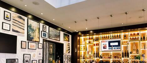 Un espace bar avec un assortiment de bouteilles d’alcool, des œuvres d’art encadrées accrochées aux murs et des sièges.