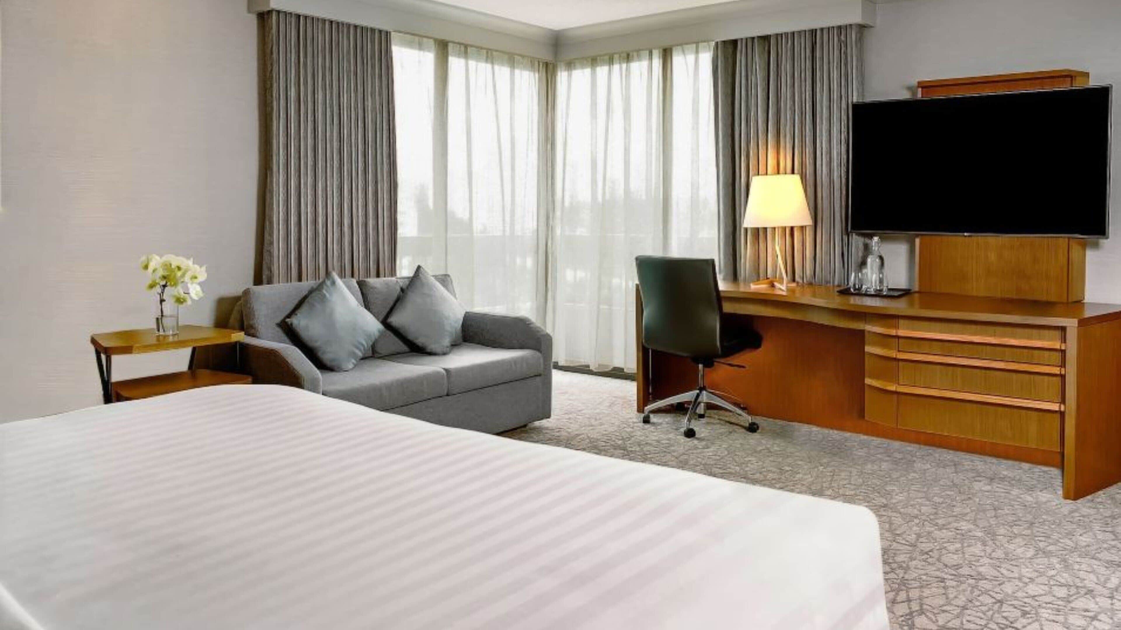 A hotel room with a large bed, a sofa, a desk with a TV, and a lamp.