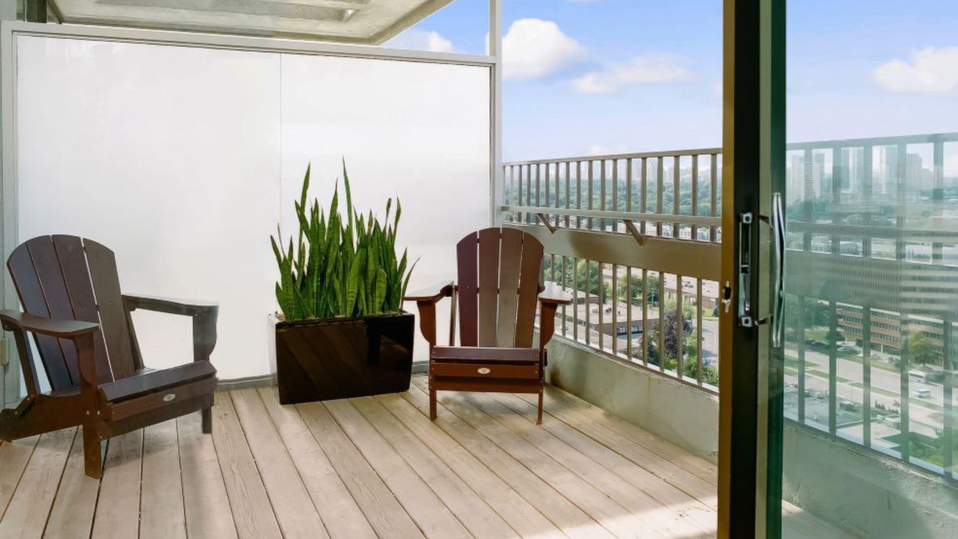 Un balcón con dos sillas Adirondack, una planta en maceta y vista a la ciudad.