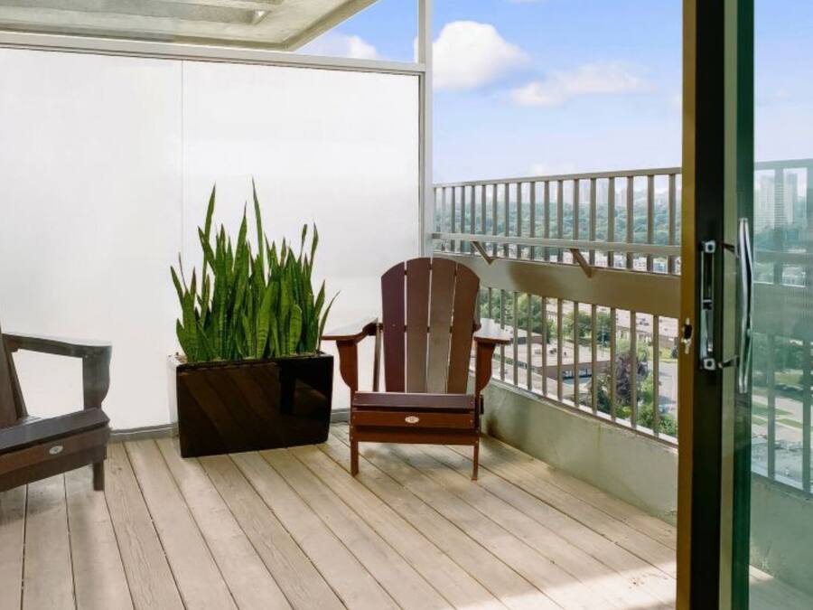 Un balcón con dos sillas Adirondack, una planta en maceta y vista a la ciudad.