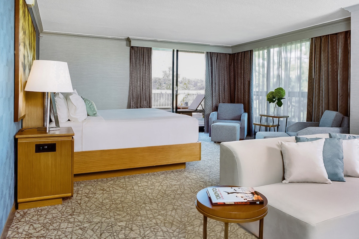 A hotel room with a bed, a sofa, a small table, a lamp, and a plant.