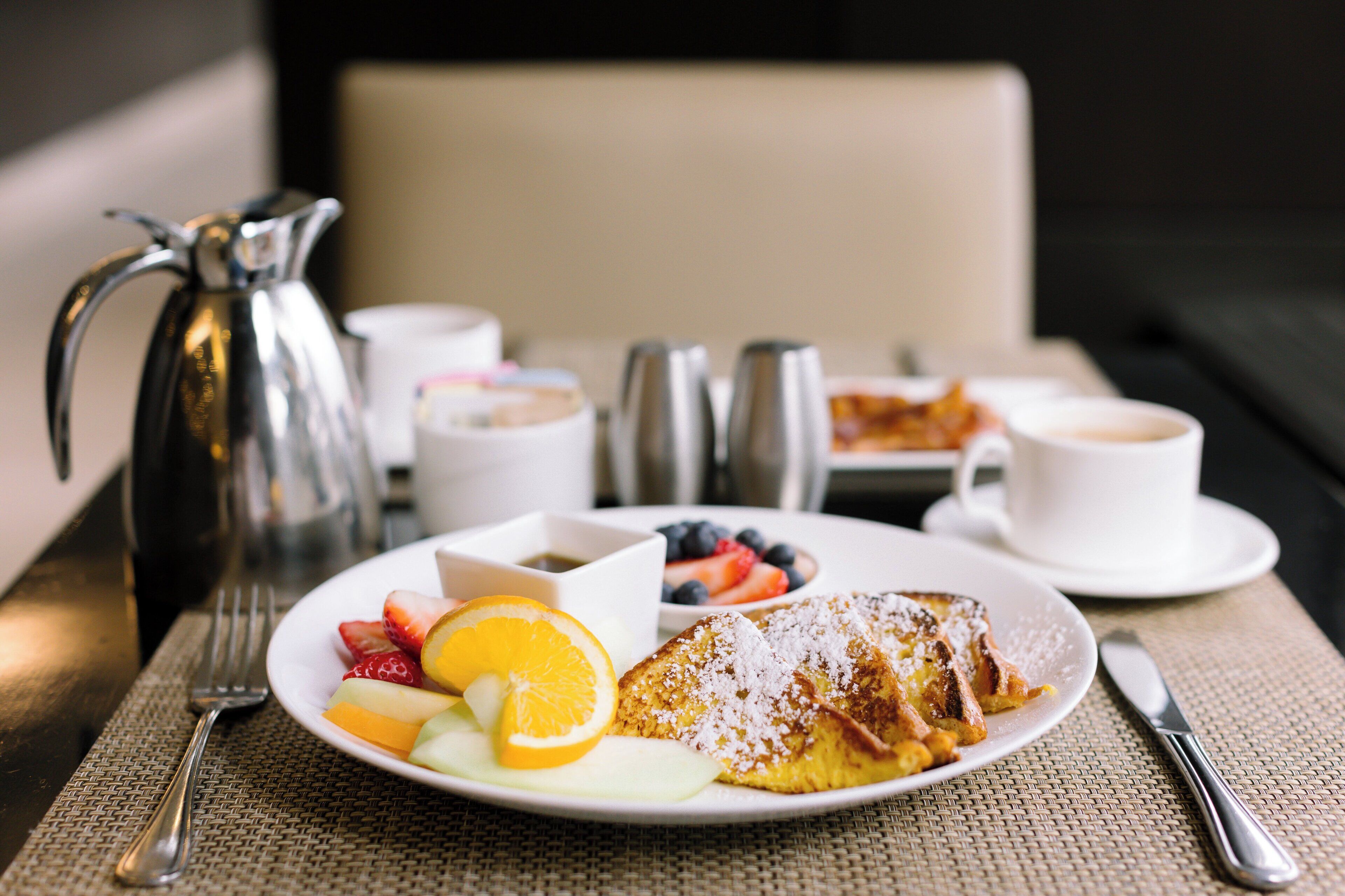 Een ontbijttafel met een bord toast, fruit en een koffiekop.