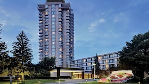 A high-rise hotel with multiple floors, a well-maintained garden, and a modern building in the foreground. - Crowne Plaza Toronto North York by IHG (Toronto)