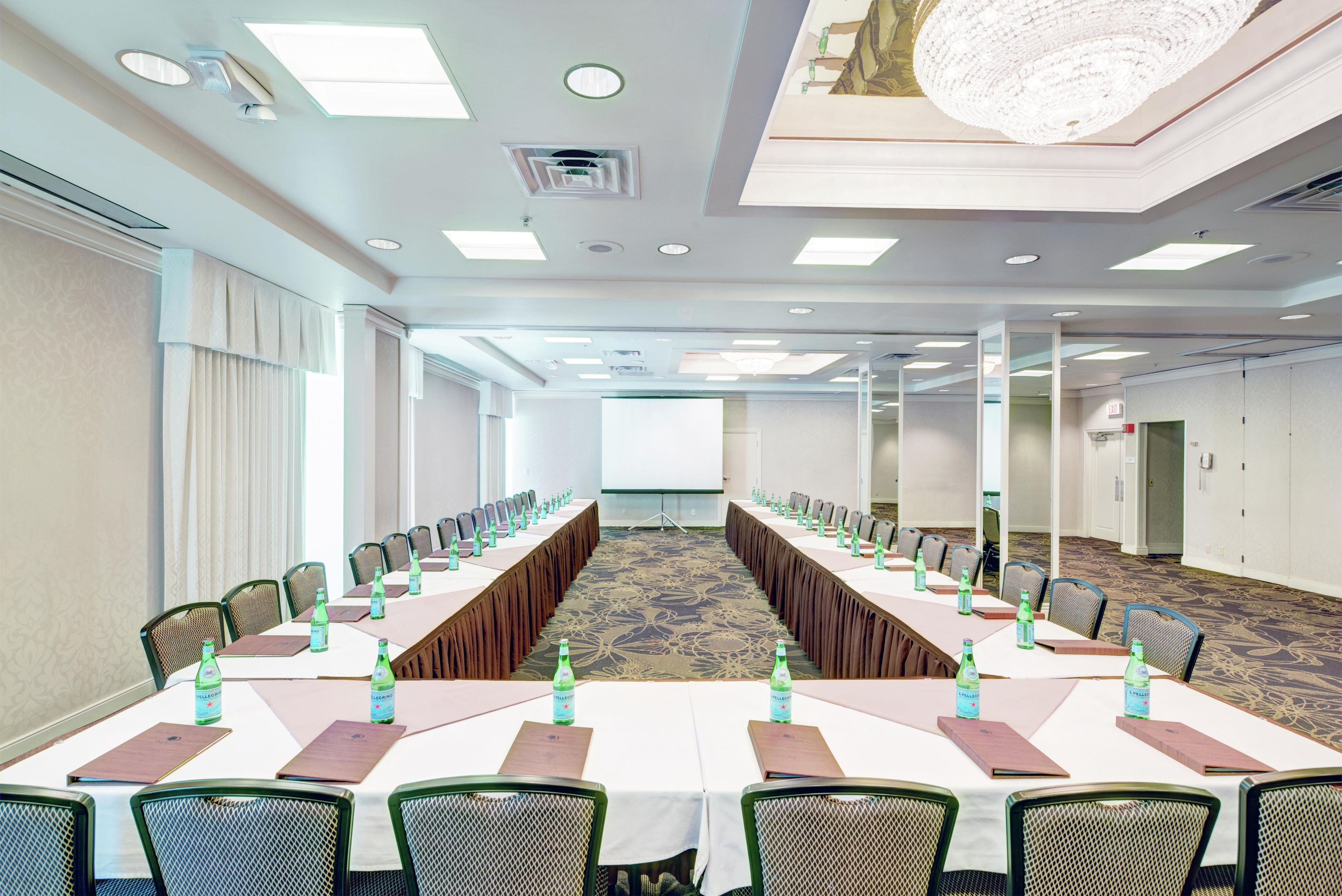A conference room with a long table, chairs, a projector screen, and a chandelier.