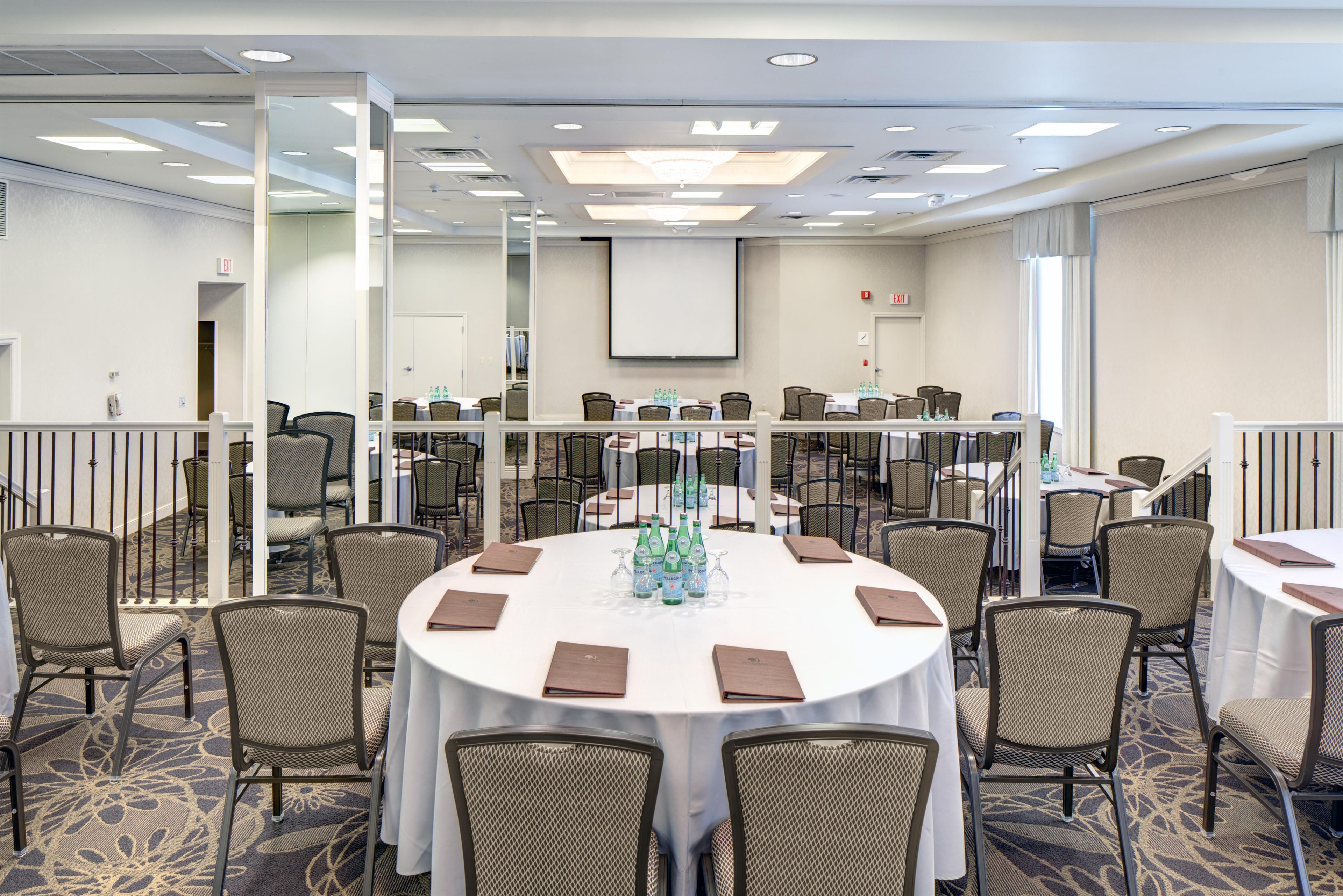 A conference room with round tables, chairs, and a projector screen.