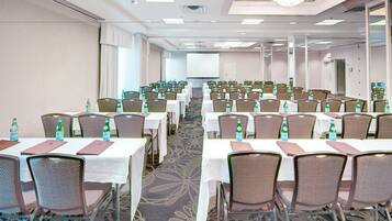 A conference room with rows of tables and chairs, each with a bottle of water.