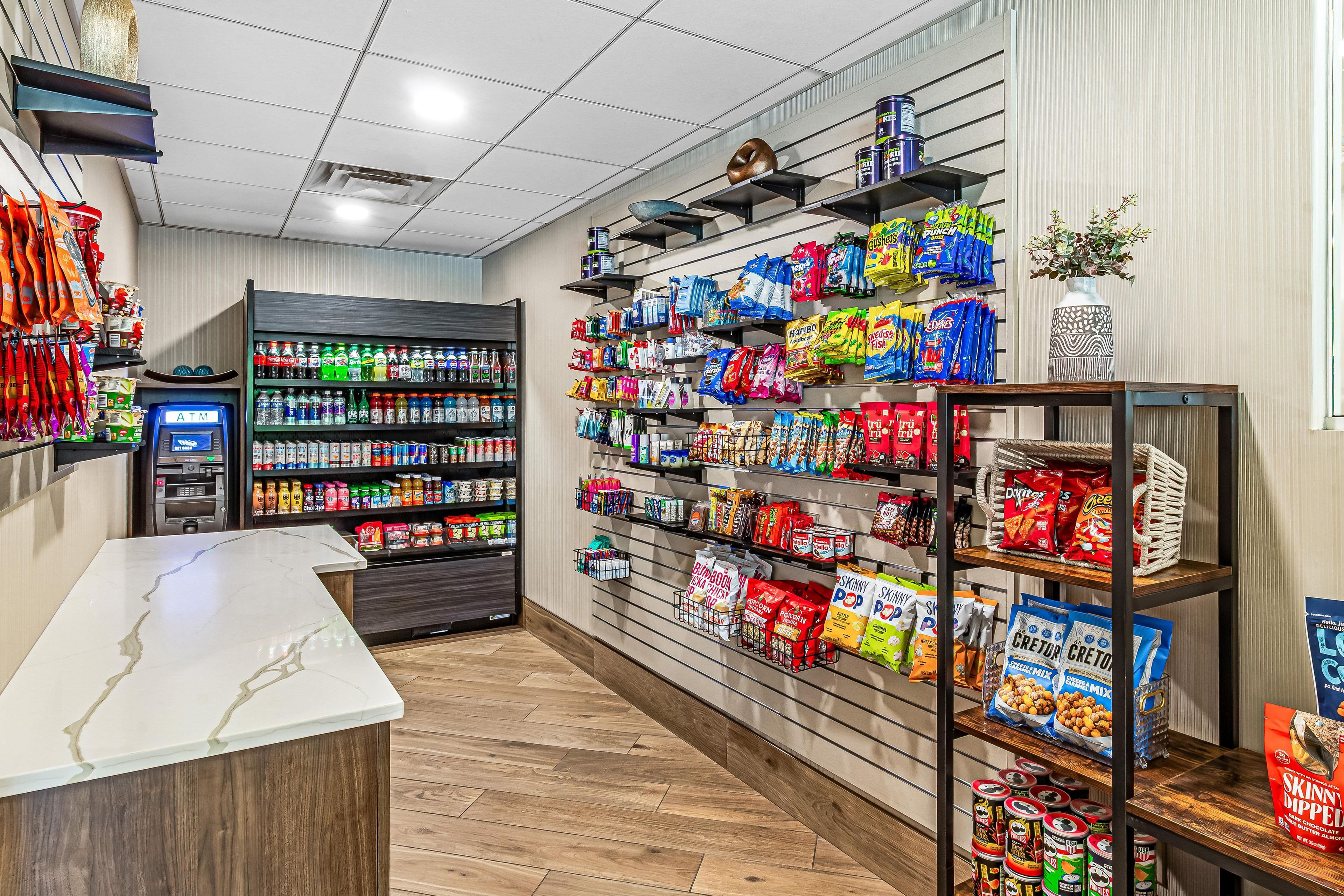 A grocery store interior with shelves stocked with snacks, a self-service beverage dispenser, and an ATM.