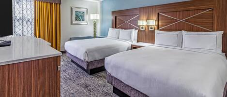 Una habitación de hotel con dos camas, un escritorio, una mesita de noche, una lámpara y una ventana con cortinas.