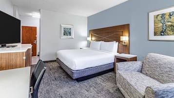 A hotel room with a bed, a desk, a chair, a TV, and a painting on the wall.