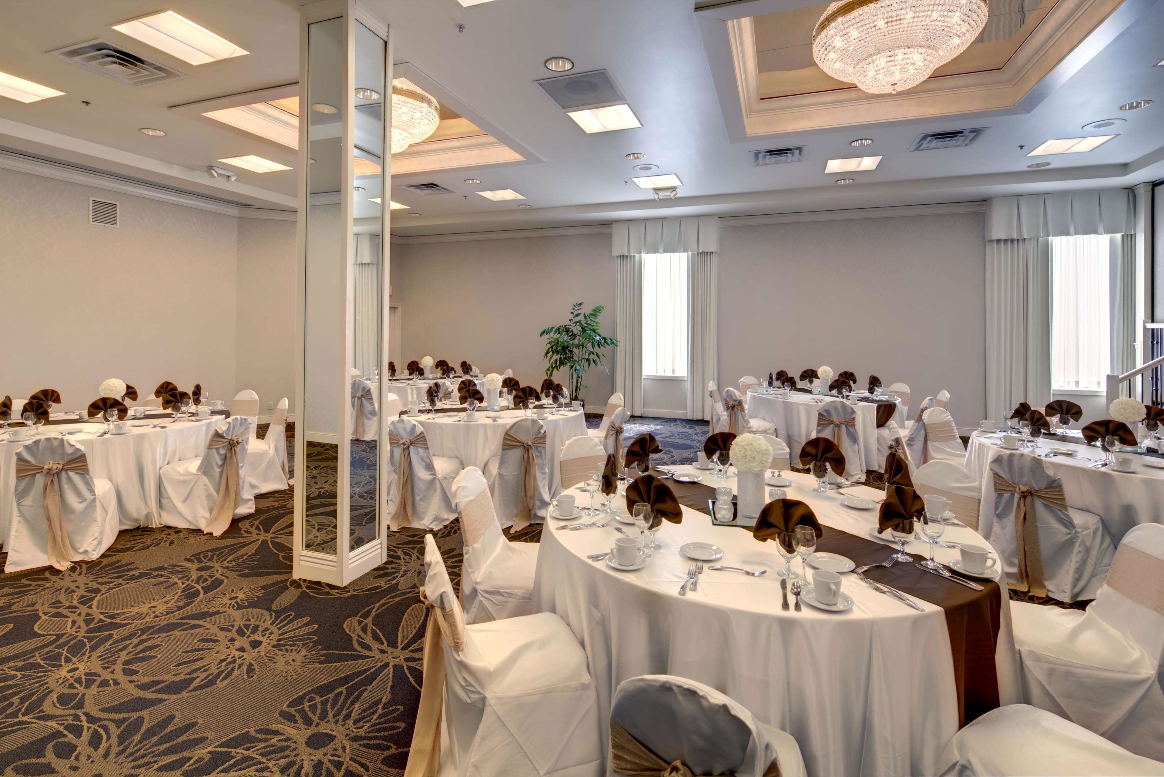 Un salón de banquetes con mesas redondas, manteles blancos y sillas cubiertas de blanco.