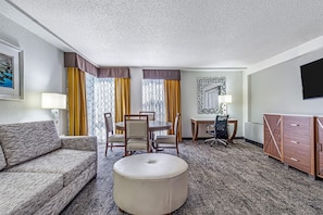 A hotel room with a sofa, round ottoman, dining table with chairs, a desk with a chair, a TV, and a wardrobe. - DoubleTree by Hilton Milwaukee Downtown (Milwaukee)
