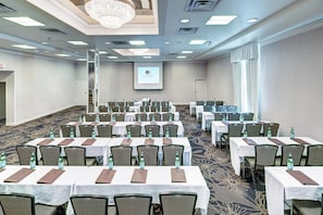 A conference room with multiple tables, chairs, and a projector screen. - DoubleTree by Hilton Milwaukee Downtown (Milwaukee)