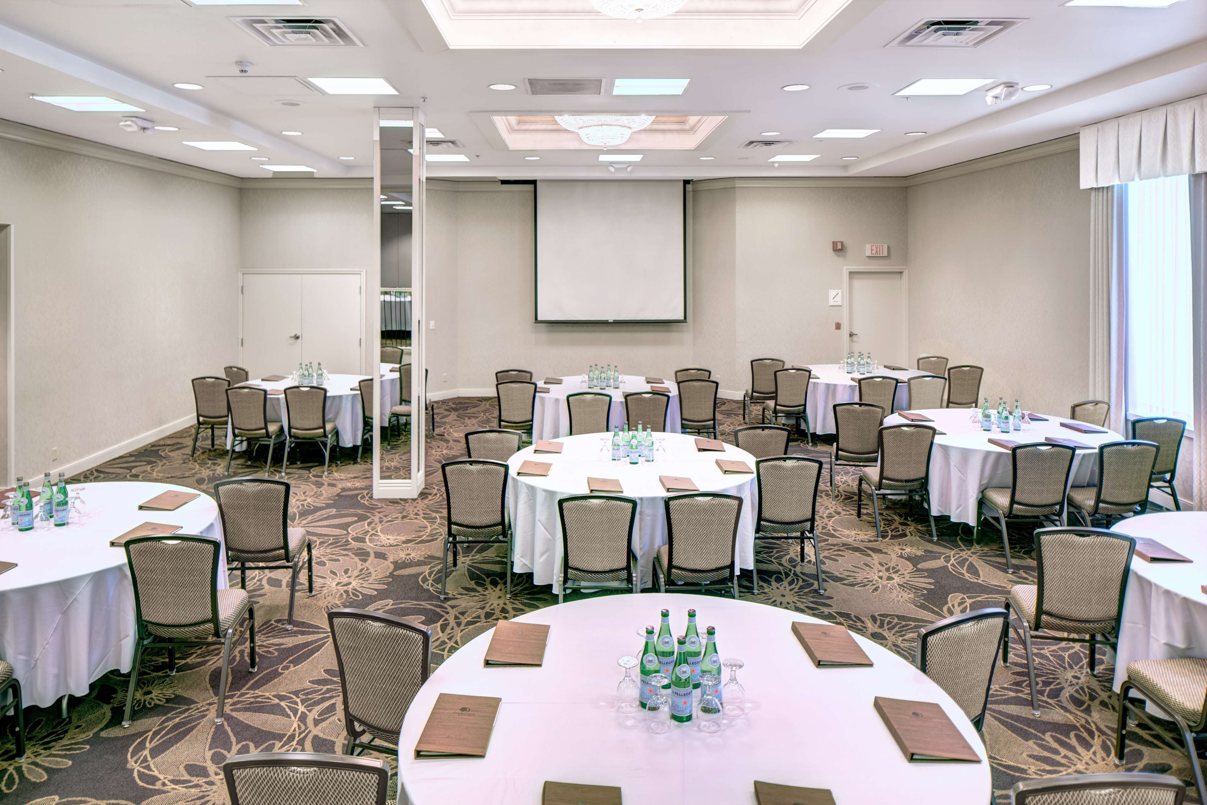 A conference room with multiple round tables, each set with chairs, water bottles, and folders.