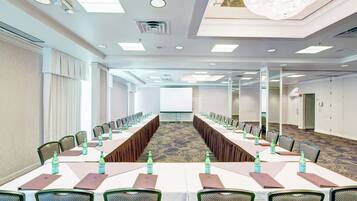 Un salón de conferencias con largas mesas, sillas y botellas de agua.