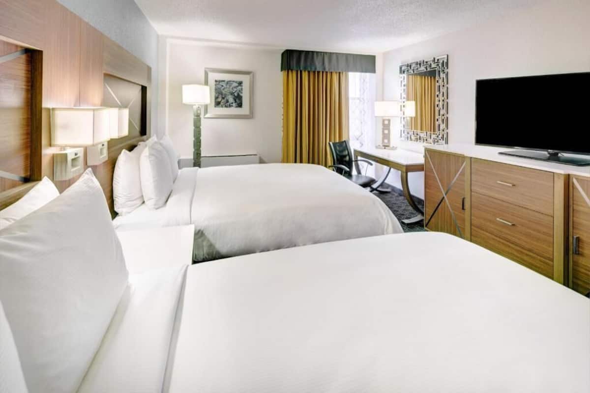 A hotel room with two beds, a desk, a chair, a television, and a window with curtains.