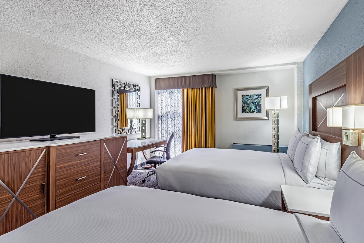 Ett hotellrum med två sängar, ett skrivbord, en tv och ett fönster med gardiner.