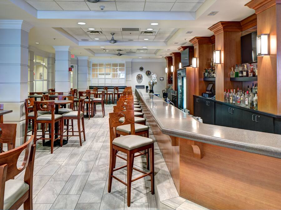 A restaurant with a long counter, wooden chairs, and a bar area with bottles.