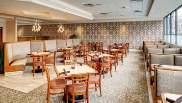 A hotel dining area with booths and tables, patterned carpet, and pendant lighting.