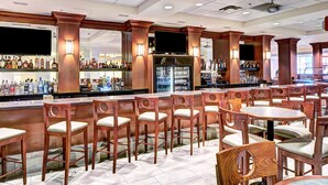 A bar area with wooden chairs and tables, a refrigerator, and shelves with bottles. - DoubleTree by Hilton Milwaukee Downtown (Milwaukee)