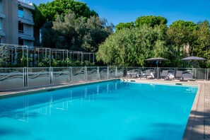 A swimming pool with a clear blue water, surrounded by a metal fence, and shaded by umbrellas. - Novotel Nice Aeroport Cap 3000 (Saint-Laurent-du-Var)