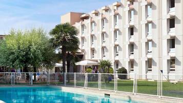 A hotel with a swimming pool, a palm tree, and a building with multiple balconies.