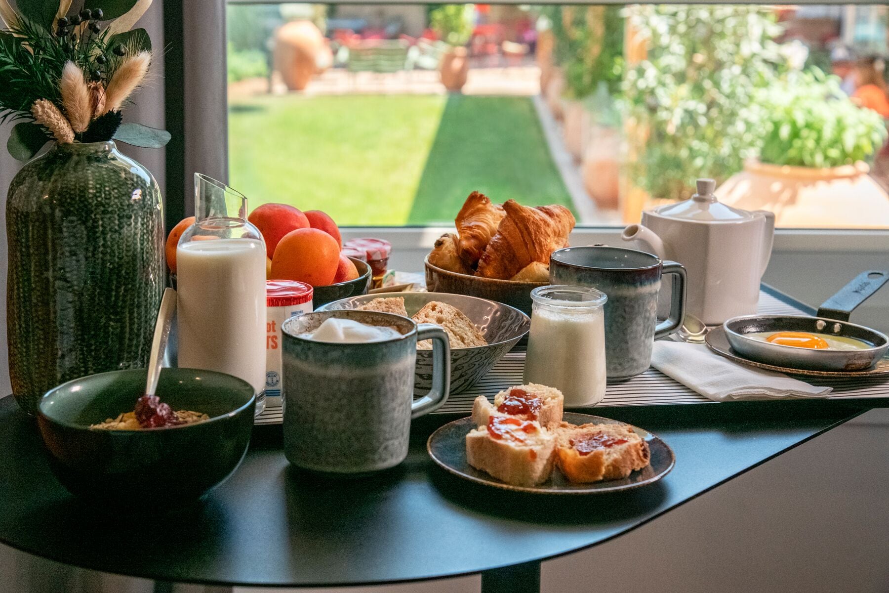 A breakfast table with various food items and drinks, including croissants, bread, and a bowl of cereal.