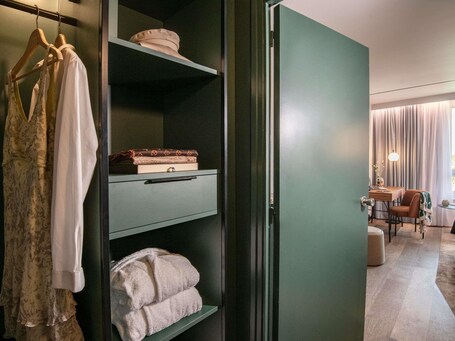 A hotel room with a wardrobe, a desk with a lamp, and a view of the outdoors.