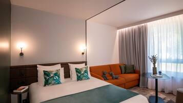 Une chambre d’hôtel avec un grand lit, un canapé orange, une petite table et une fenêtre avec des rideaux.