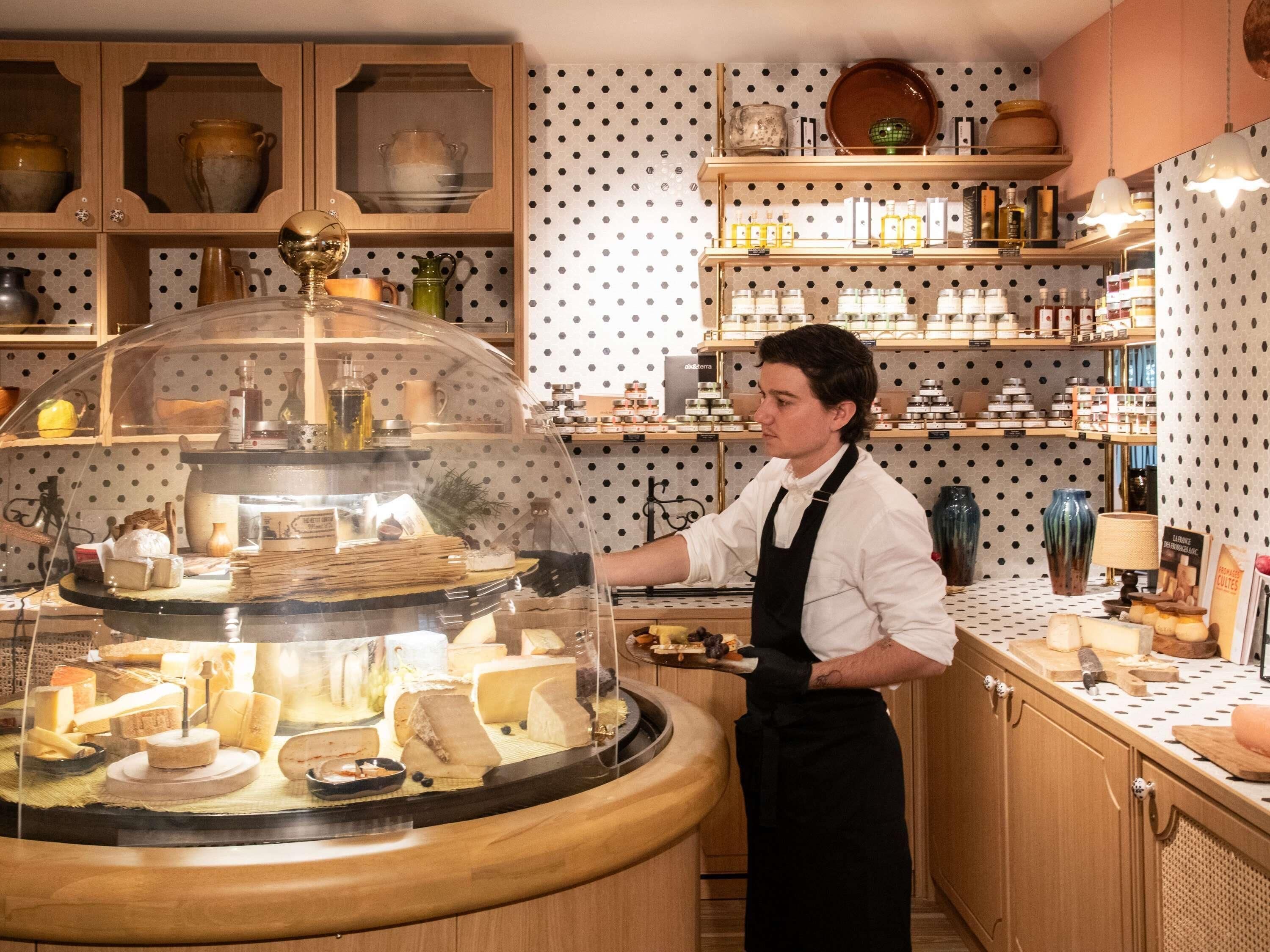 A cheese display with a glass dome, surrounded by wooden shelves with various items.