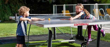 Deux enfants jouent au ping-pong à l’extérieur, sur une table mobile équipée de roulettes.