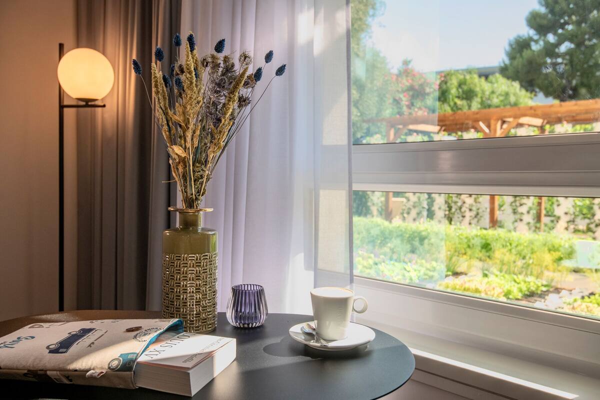 A table with a book, a cup of coffee, a decorative vase with dried plants, and a lamp.