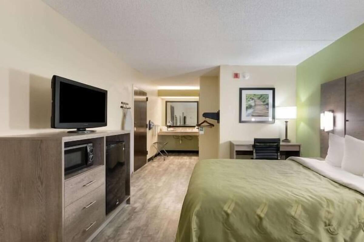 Ein Hotelzimmer mit Bett, Fernseher, Schreibtisch und Bad.