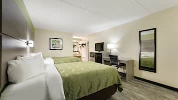 A hotel room with two beds, a desk, a chair, a TV, and a mirror.