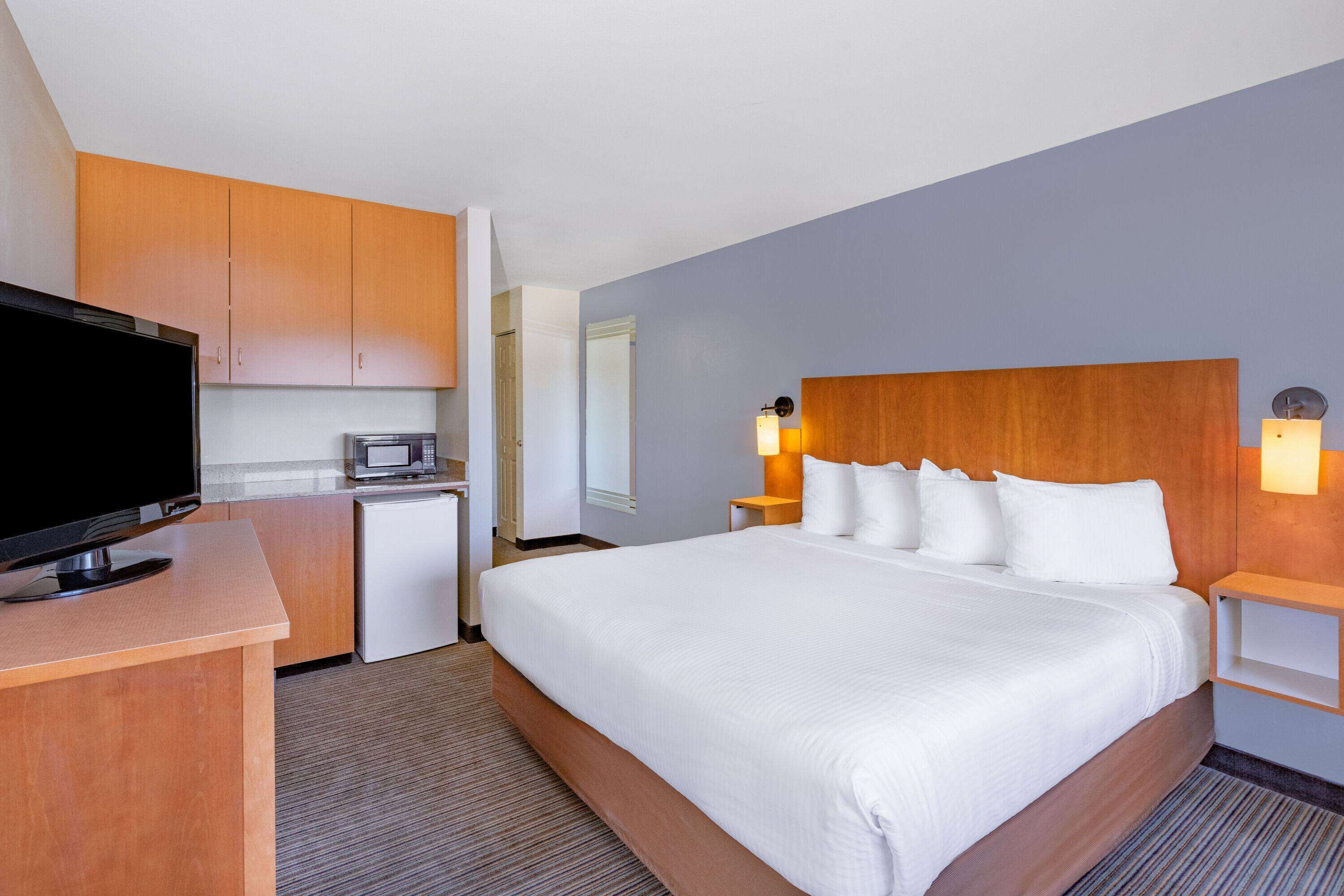 A hotel room with a large bed, a TV, a microwave, and wooden cabinets.