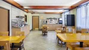 A restaurant with wooden tables and chairs, a kitchen area, and a television. - La Quinta Inn & Suites by Wyndham Helena (Helena)