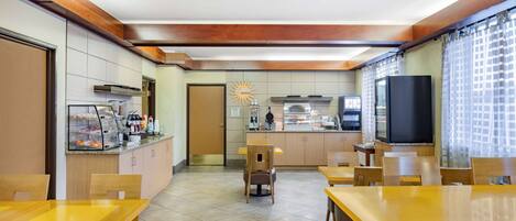 Un restaurante con mesas y sillas de madera, una zona de cocina y un televisor.