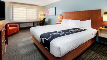 A hotel room with a large bed, a desk, a chair, and a TV.