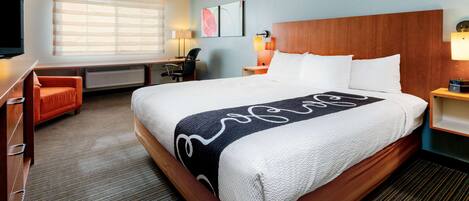A hotel room with a large bed, a desk, a chair, and a TV.