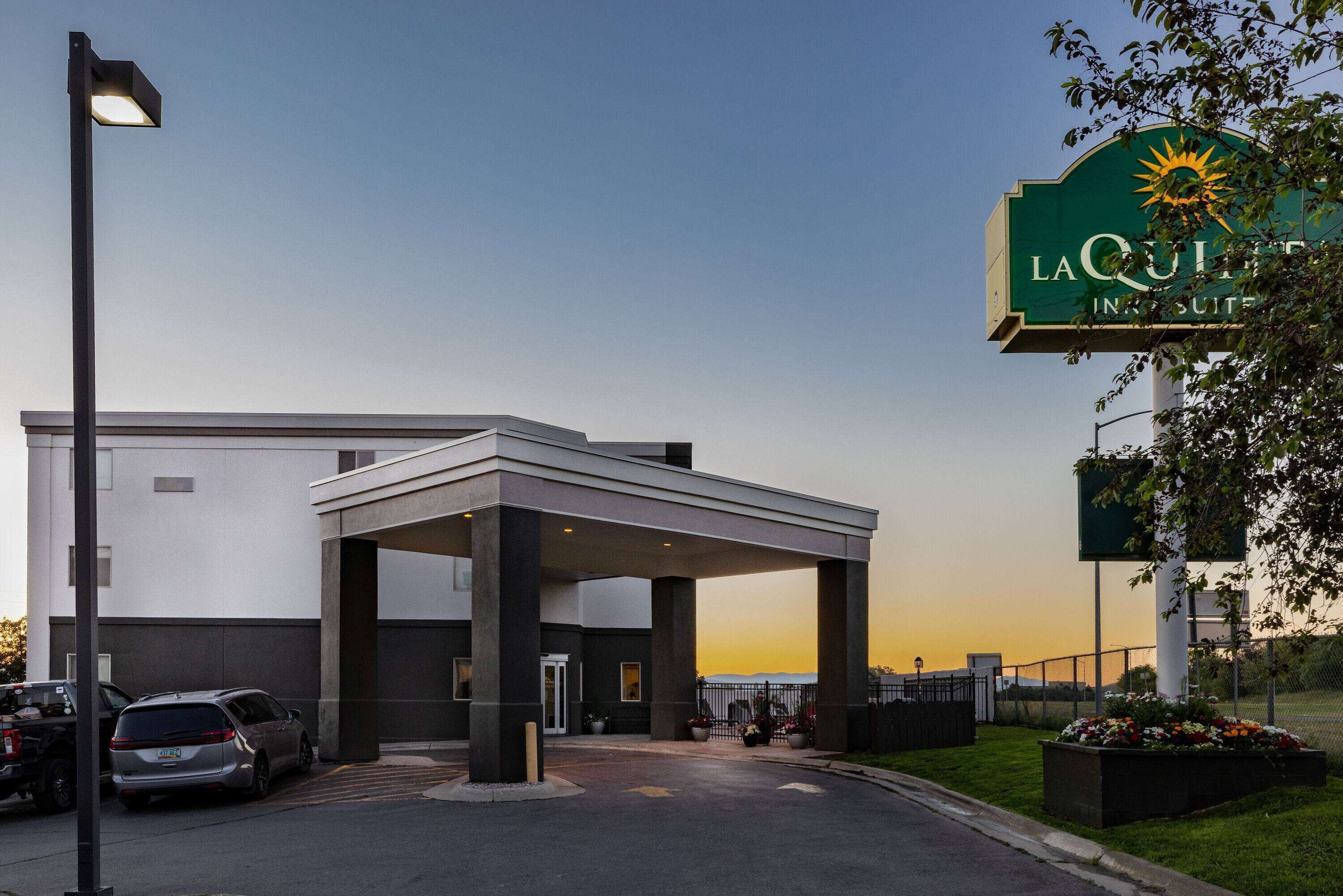 A hotel entrance with a covered waiting area, a parking lot, and a sign indicating it's a LaQuinta Inn & Suites.