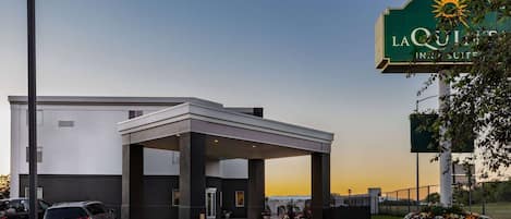 A hotel entrance with a covered waiting area, a parking lot, and a sign indicating it's a LaQuinta Inn & Suites.